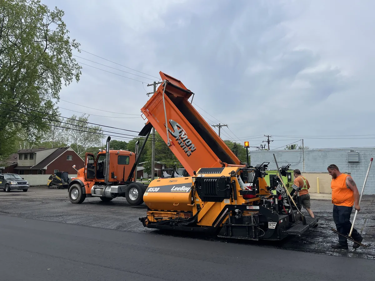 Simon Paving dump truck feeding hot asphalt into a LeeBoy paver while the crew works the mat