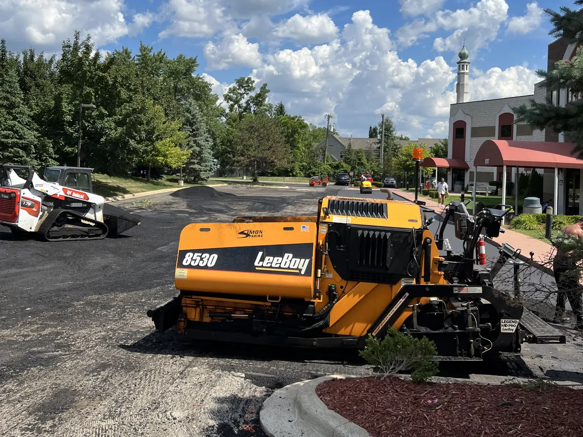 Asphalt paver working along a curb to rebuild a worn commercial lot